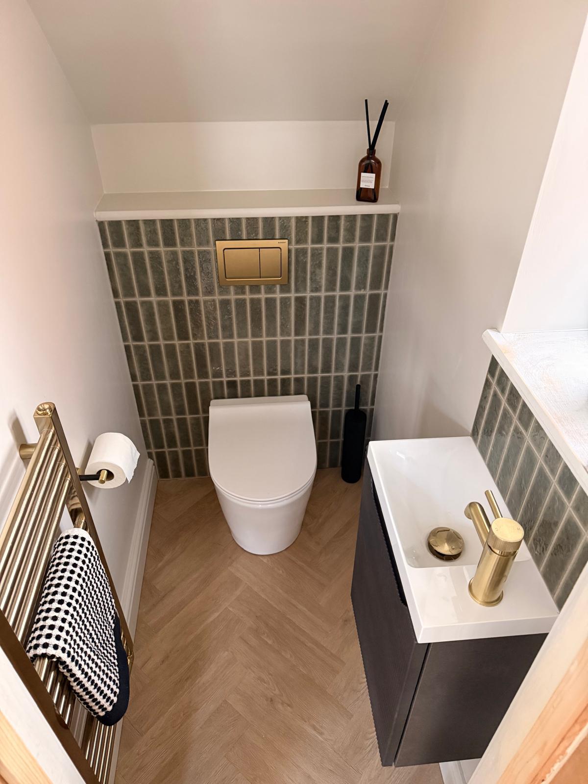 Finished cloakroom with green mosaic tiles, brass flush plate and wall-hung toilet
