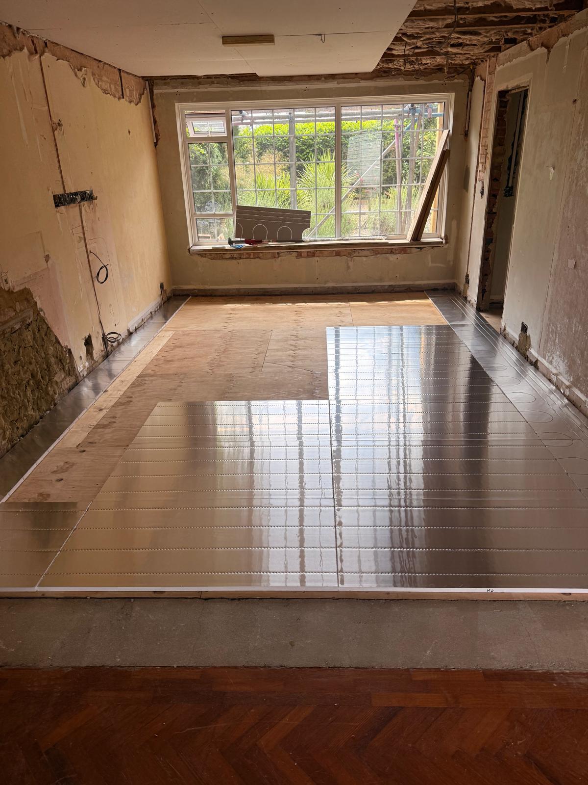 Grooved underfloor heating panels laid in a stripped-back room